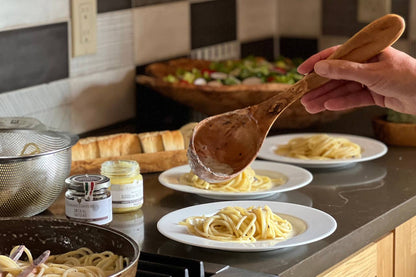 Person holding an Italian Olivewood Soup and Pasta Ladle over a plate of pasta