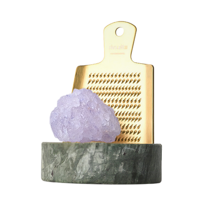 Small gold grater with a purple crystal on a gray base against a white background
