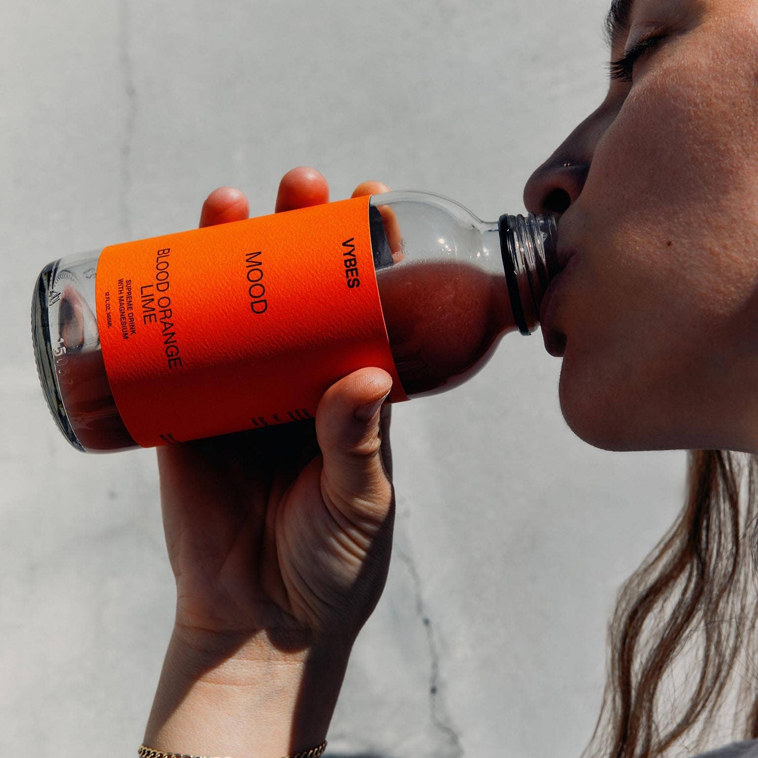 Person drinking from a bottle with an orange label against a neutral background