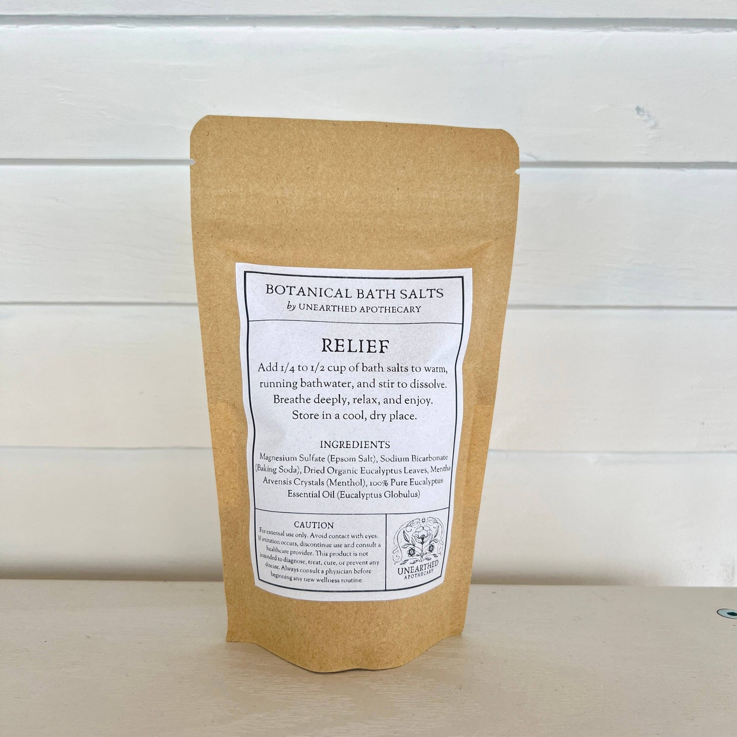 Kraft paper packaging of botanical bath salts with a label on a wooden surface.