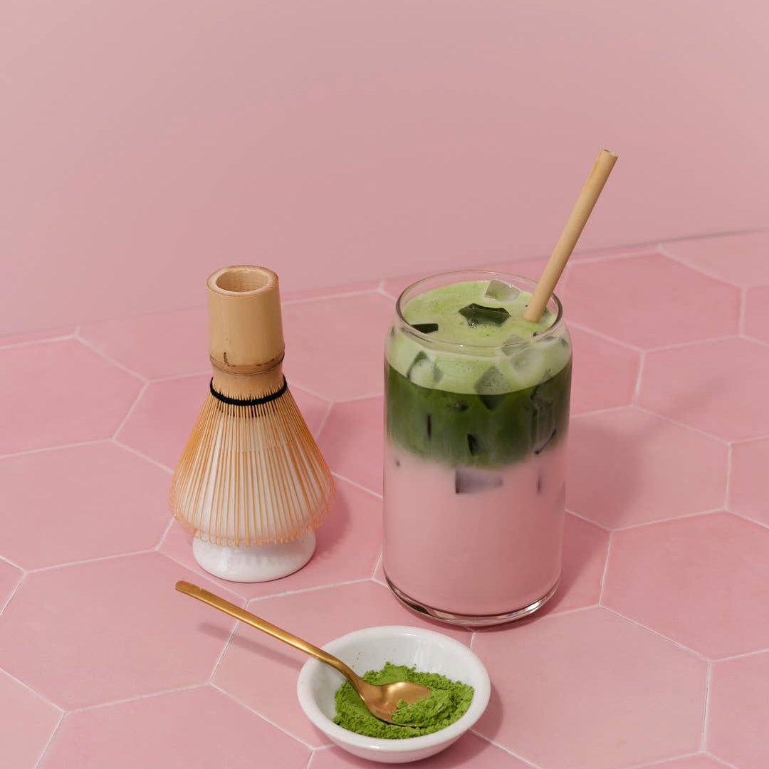 Matcha green tea set with glass, whisk, and bowl on a pink tiled background