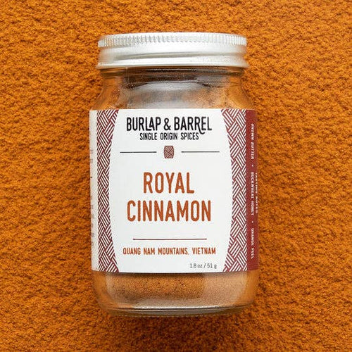 A jar of Burlap & Barrel Royal Cinnamon single origin spice on a textured orange background.