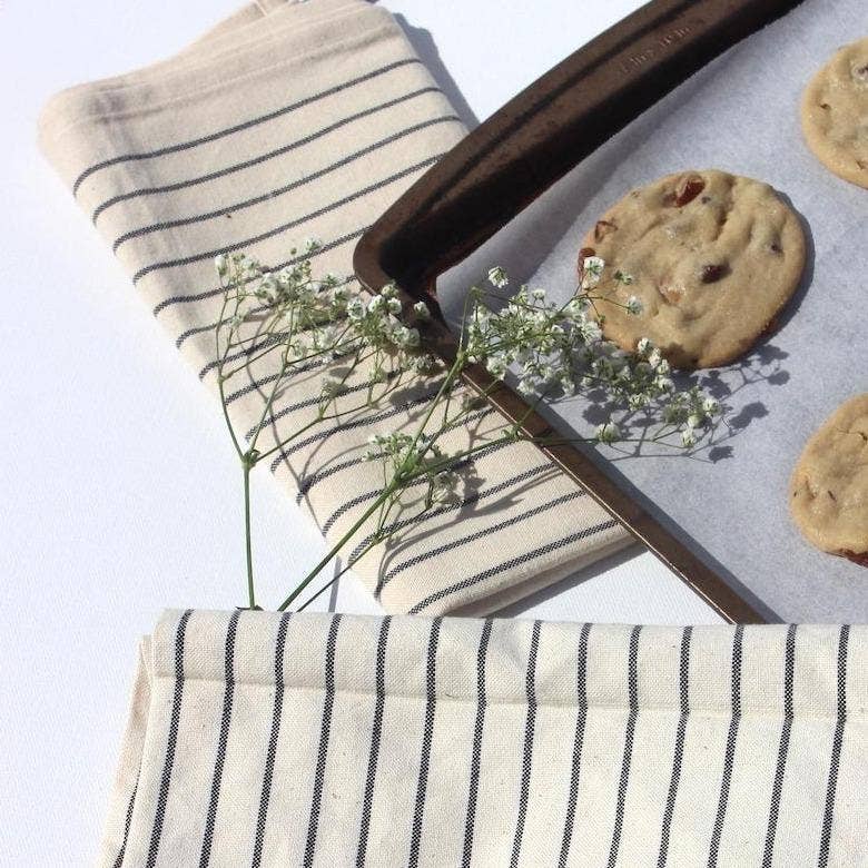 Baking tray with cookies on a white surface, next to a striped cloth and small plant.