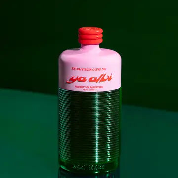 A bottle of Ya Albi extra virgin olive oil, featuring a pink upper label and cap with a ribbed green glass body, set against a dark green background.