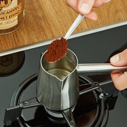 Person adding coffee grounds to a portafilter on a stove with a Mehu coffee can in the background.