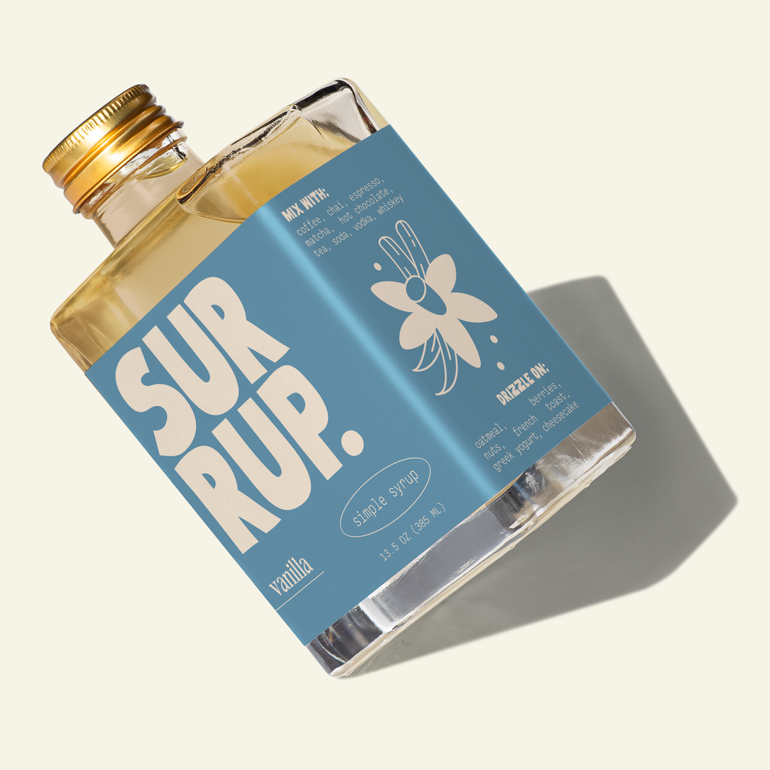 A bottle of SURRUP. vanilla syrup with a light blue label and gold cap, shown at an angle on a cream background with a soft shadow.