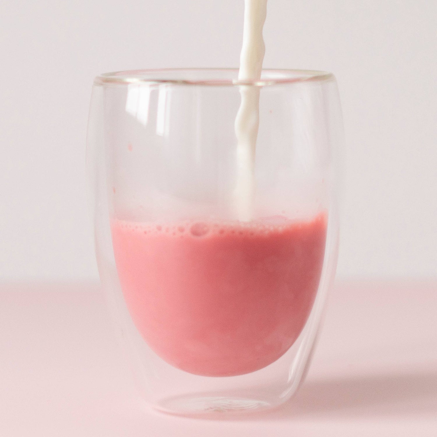 Pink liquid being poured into a clear glass with a white background