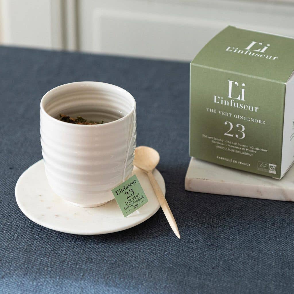 White ceramic cup with tea leaves, a wooden spoon, and a green box labeled &
