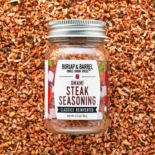 Jar of Burlap & Barrel Umami Steak Seasoning on a background of spice mix