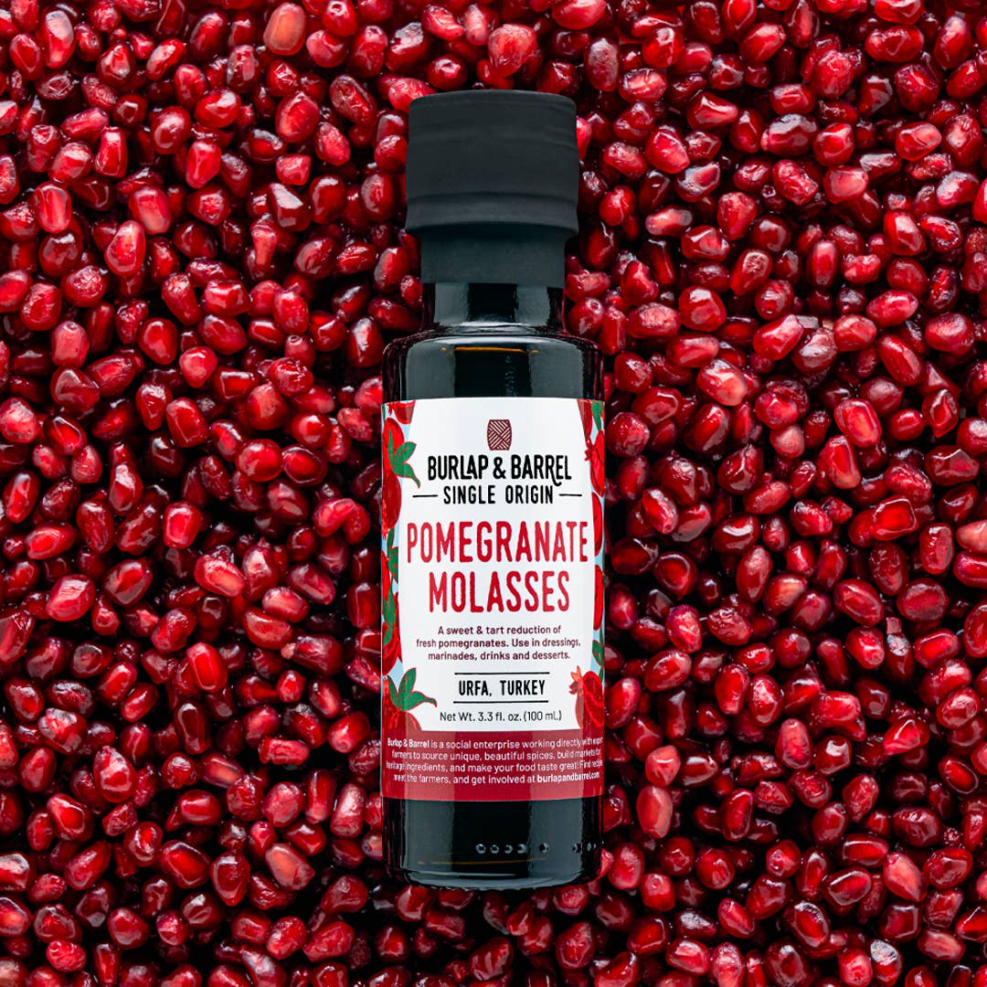 Bottle of Burlap &amp; Barrel Pomegranate Molasses against a background of pomegranate seeds