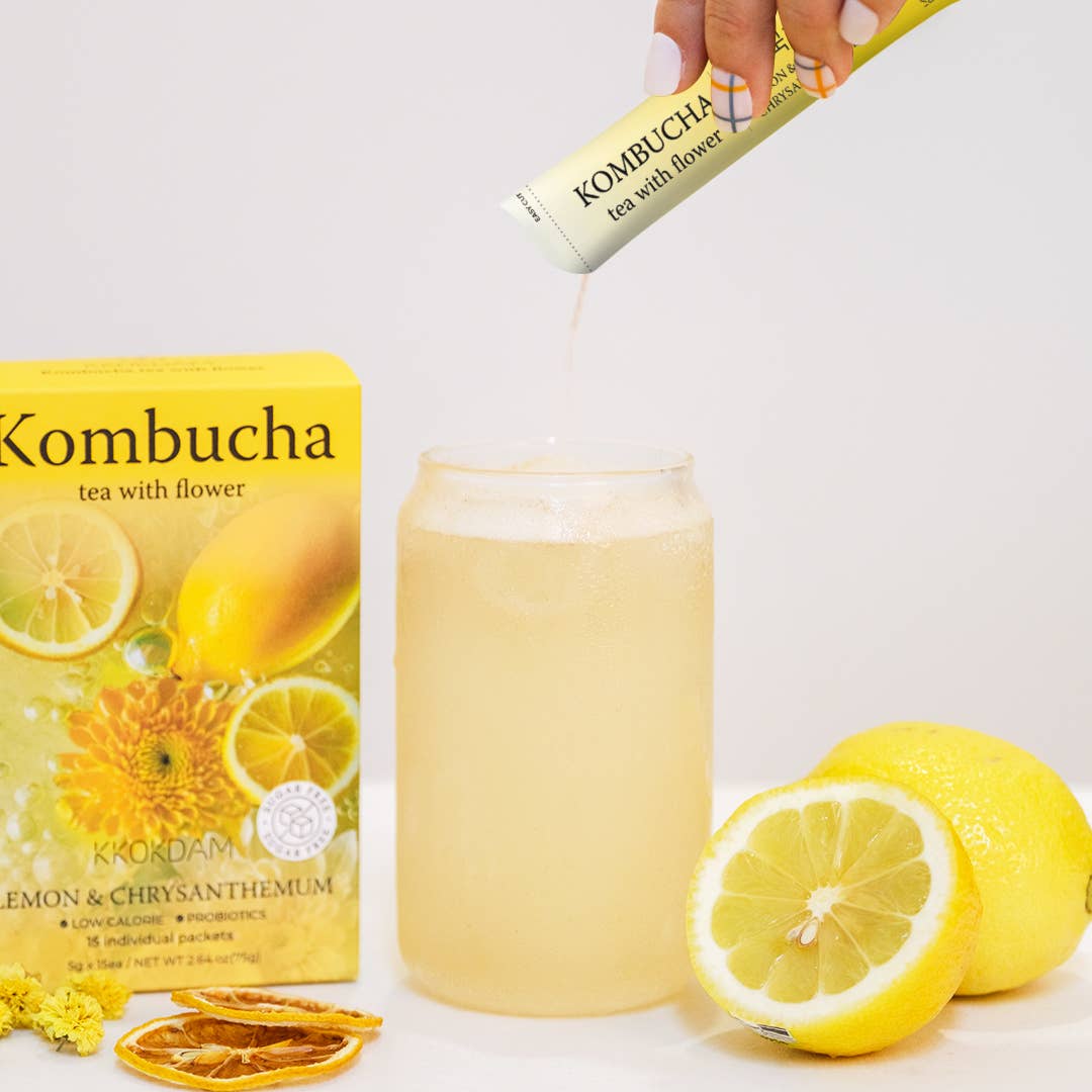 Kombucha tea being poured into a glass with lemon slices and a box of kombucha in the background.