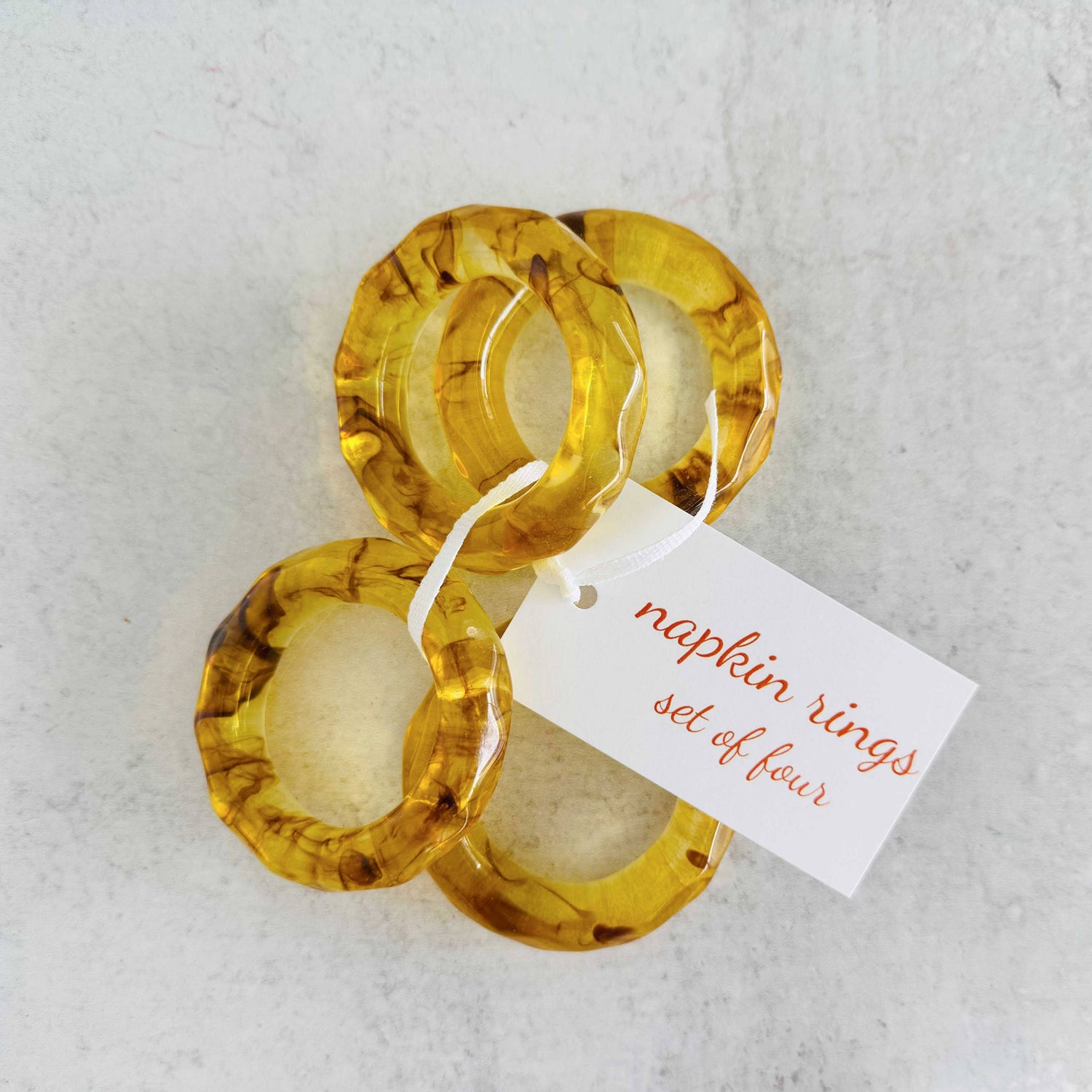 Set of four amber-colored napkin rings with a tag on a light gray background