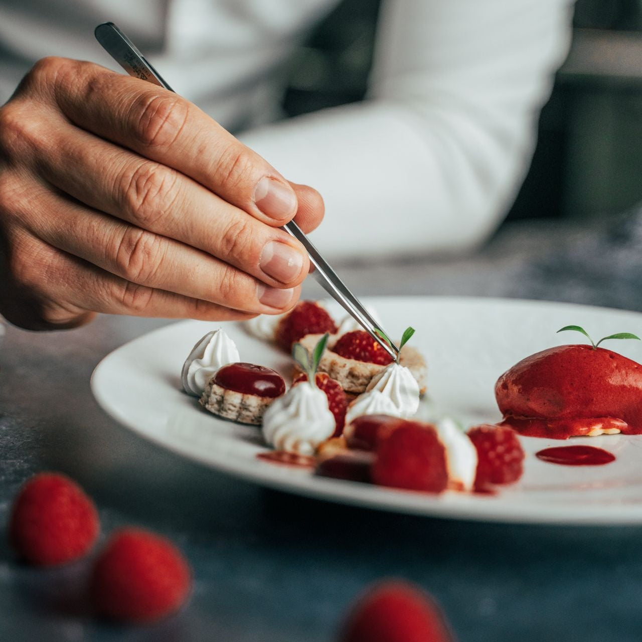 Person garnishing a dessert with a fork on a plate, surrounded by raspberries.