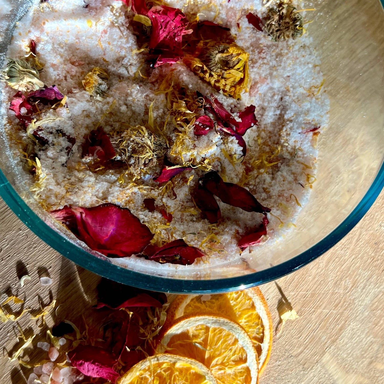 Bowl with bath salts, rose petals, and orange slices on a wooden surface