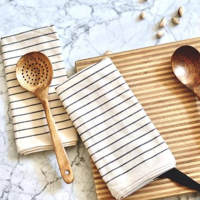 Wooden spoon and cutting board with striped towels on a marble surface