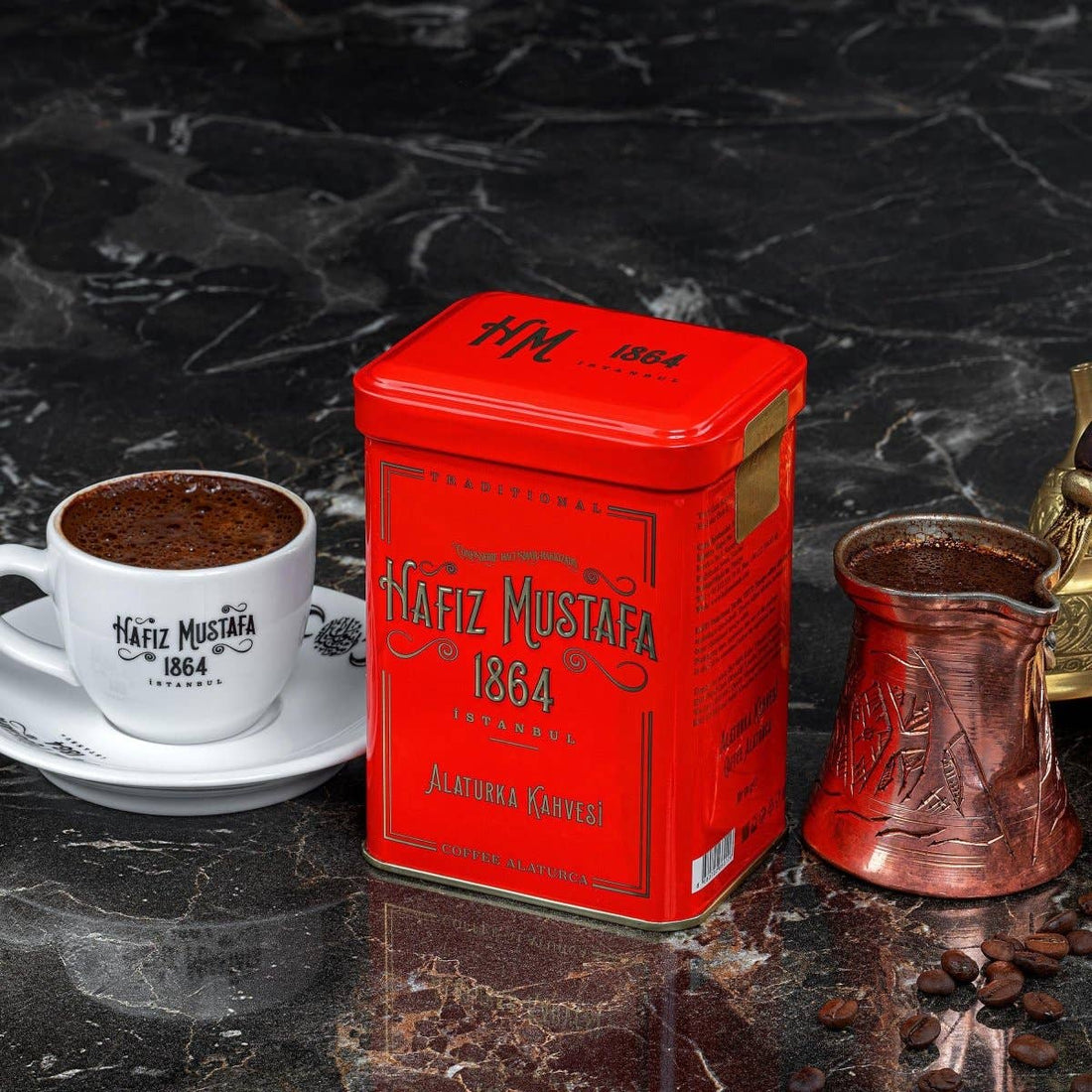 Red Nafiz Mustafa coffee tin with a cup of coffee and a copper coffee pot on a dark marble surface.