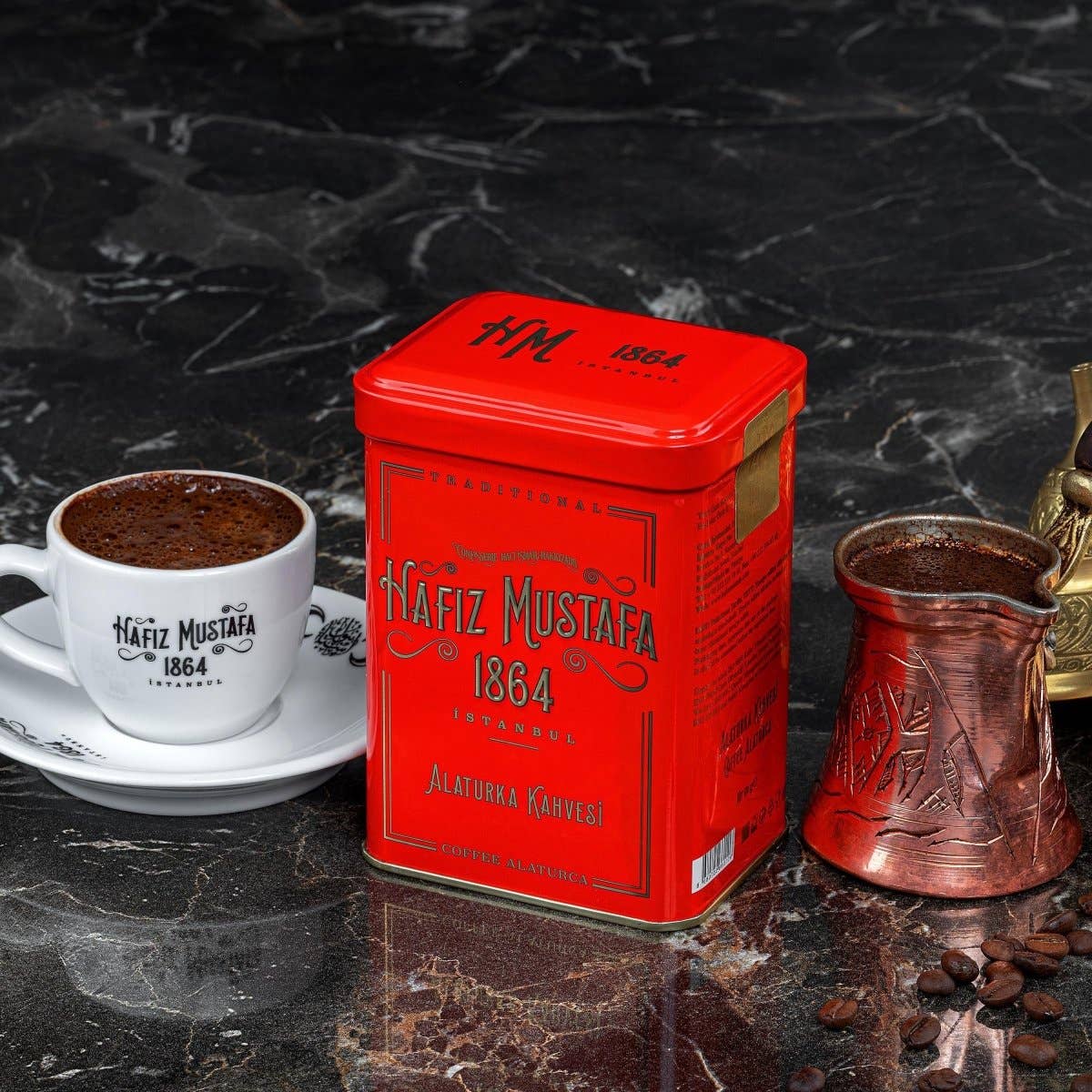 Red Nafiz Mustafa coffee tin with a cup of coffee and a copper coffee pot on a dark marble surface.
