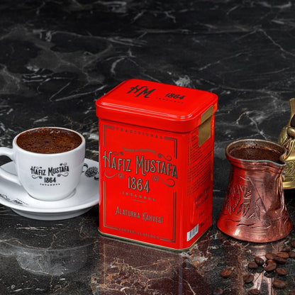 Red Nafiz Mustafa coffee tin with a cup of coffee and a copper coffee pot on a dark marble surface.