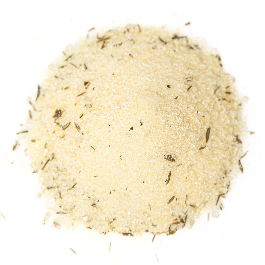 A small mound of lemon-thyme sugar &amp; salt cocktail rimmer with visible dried herb flecks, photographed from above on a plain white background.