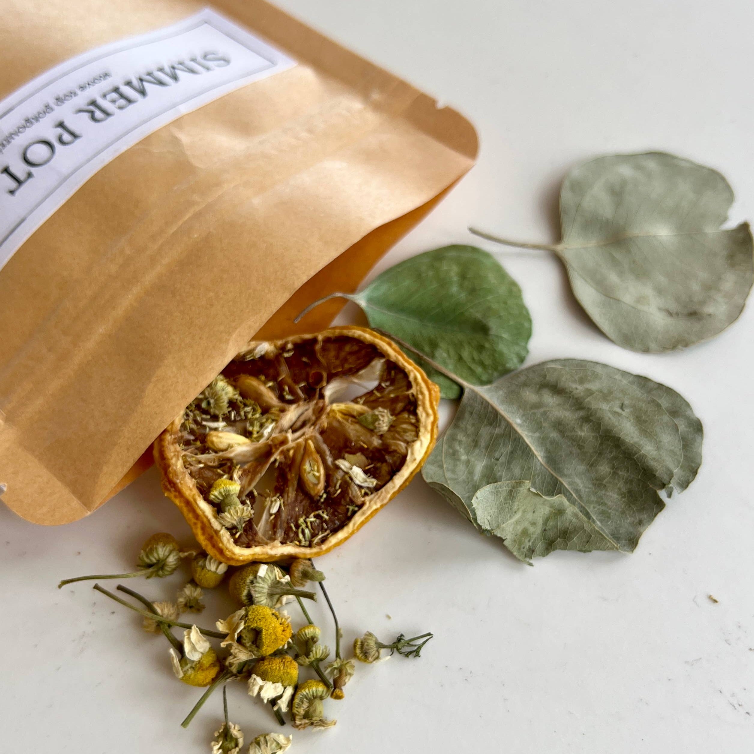 Herbal tea packaging with dried herbs and leaves on a white surface