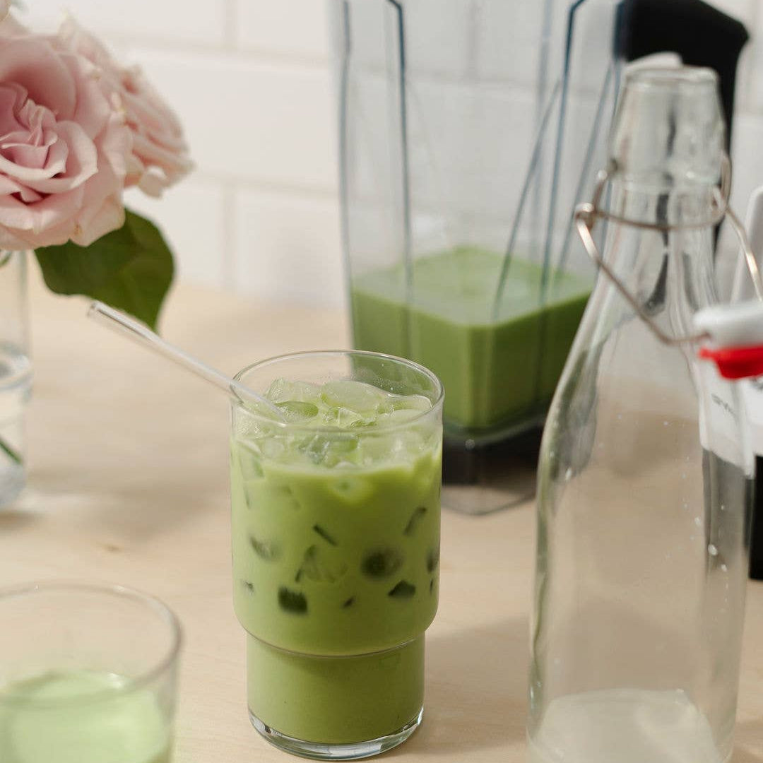 Green iced drink in a glass with a blender and bottle in the background
