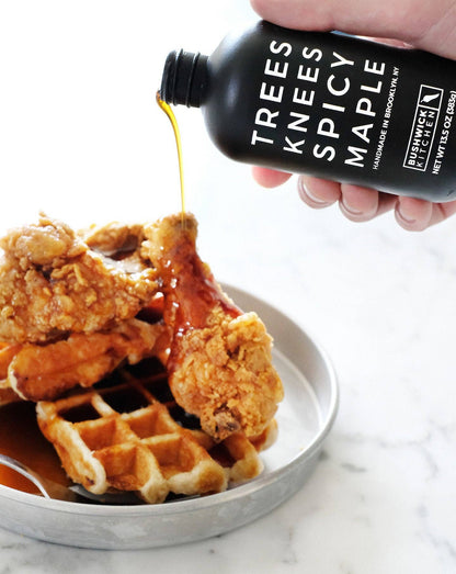 Fried chicken and waffles with a bottle of Trees Knees Spicy Maple syrup being poured over them.