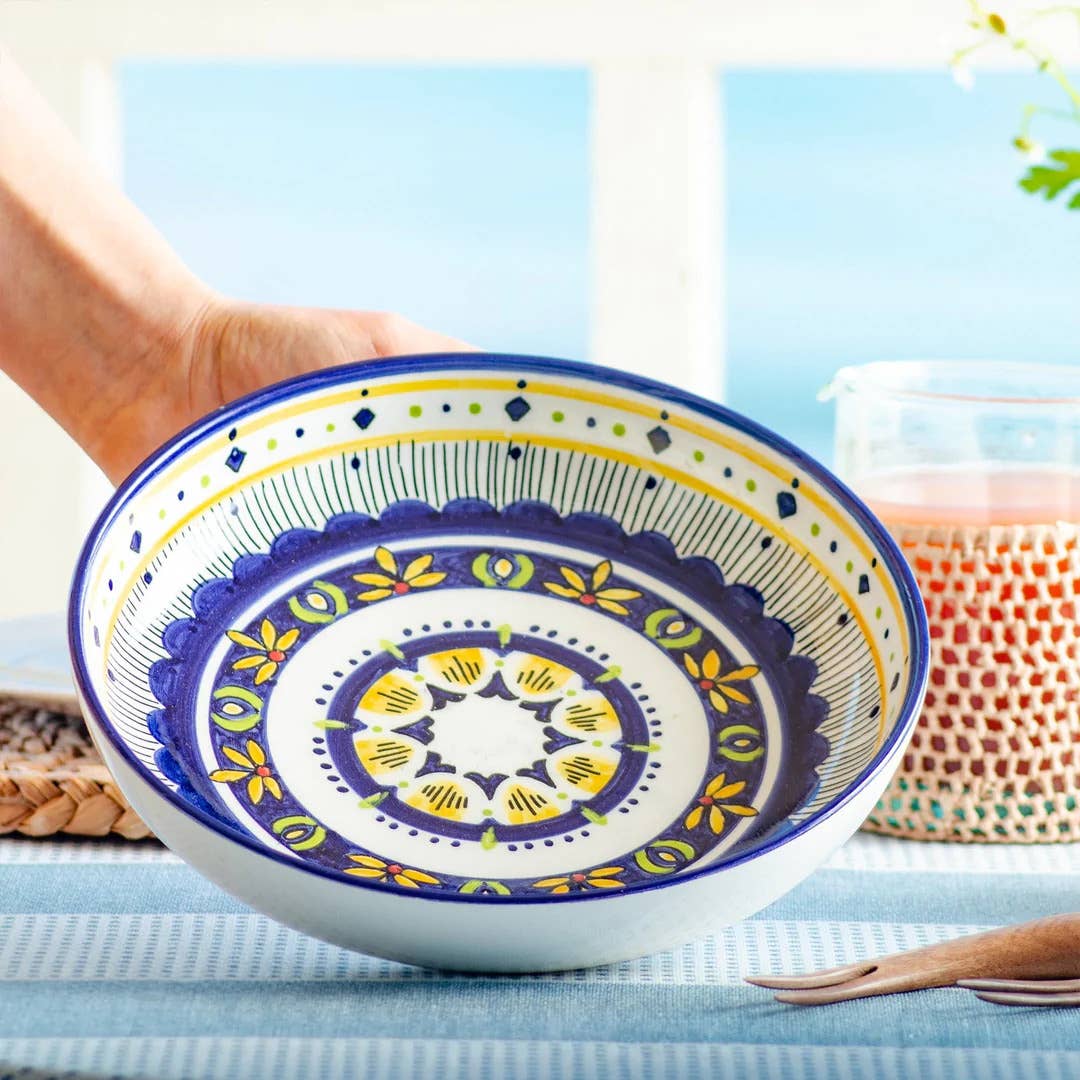 Decorative ceramic plate with colorful patterns held by a hand on a light blue background.