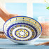 Decorative ceramic plate with colorful patterns held by a hand on a light blue background.