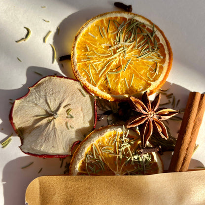 Dried oranges, apples, cinnamon sticks, and star anise on a white surface with a wooden box.