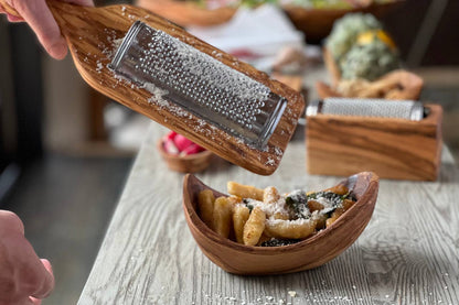Wooden grater being used to sprinkle cheese over a dish of gnocchi