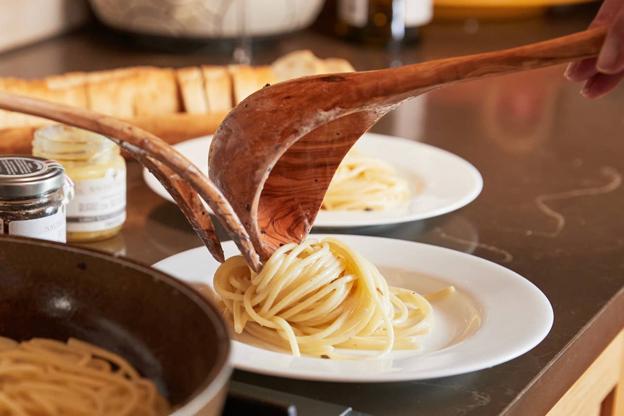 Person serving pasta from an Italian Olivewood Soup and Pasta Ladle onto a white plate