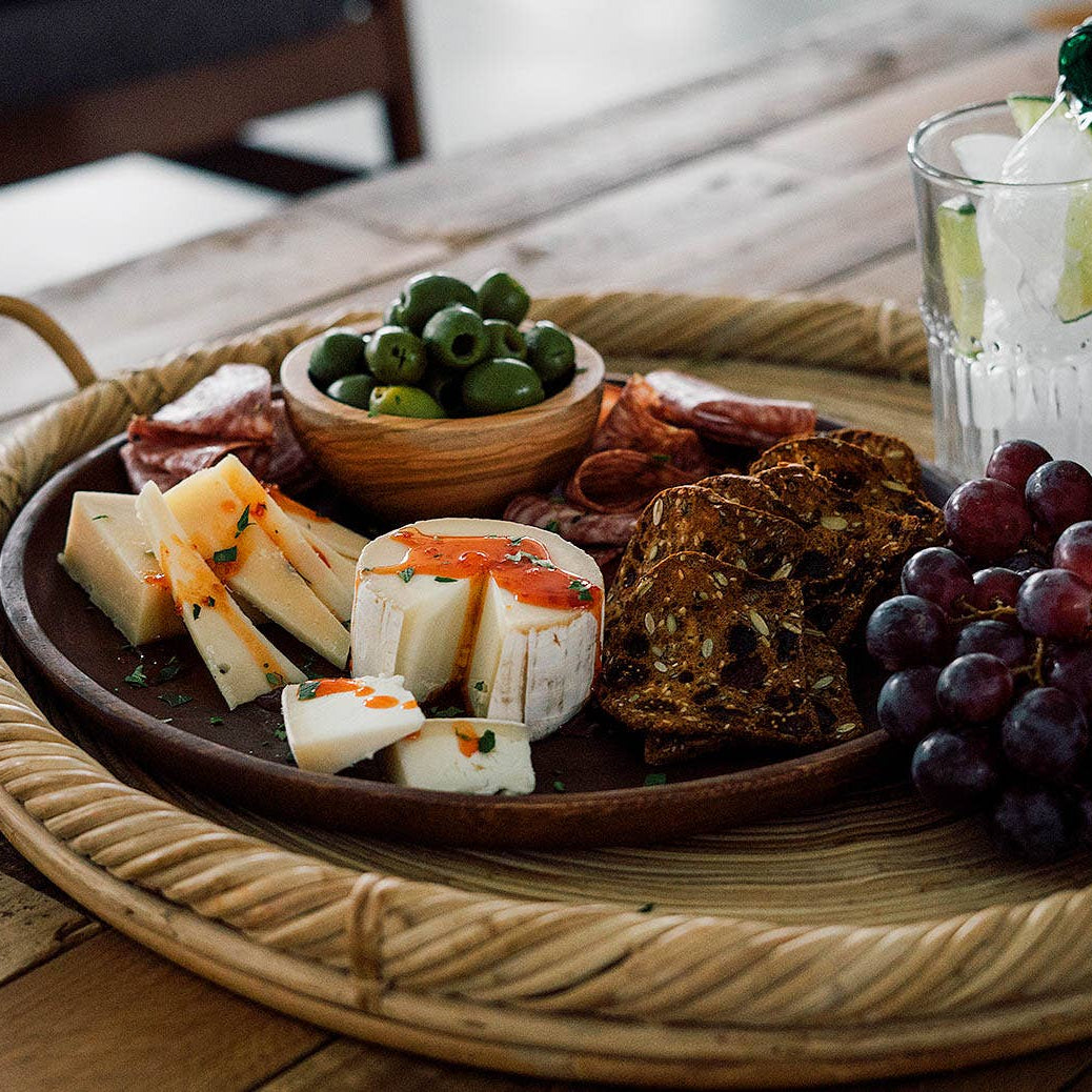 Platter of assorted cheeses, fruits, and olives on a wooden table with a glass of water and a bottle of wine.