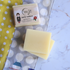 Two bars of soap on a polka dot towel with a yellow cloth and a soap packaging in the background.
