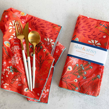 Red floral-patterned napkins with gold and silver cutlery on a light gray background