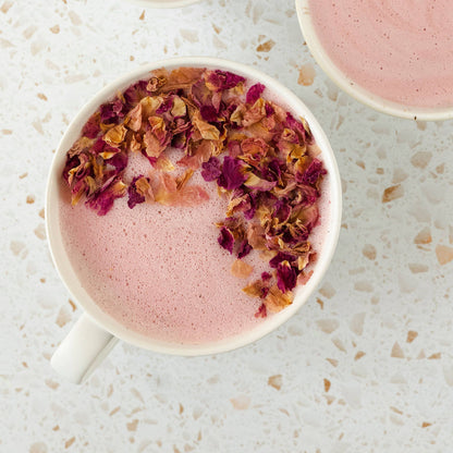 Pink drink with edible flowers in a white mug on a light textured surface