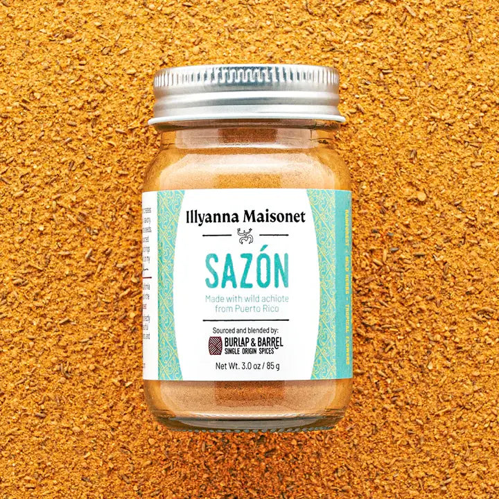 Jar of Ilyanna Maisonet Sazón spice blend on a textured orange background