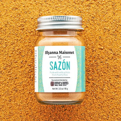 Jar of Ilyanna Maisonet Sazón spice blend on a textured orange background