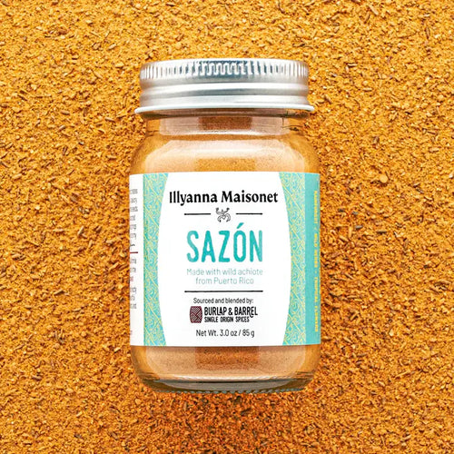 Jar of Ilyanna Maisonet Sazón spice blend on a textured orange background