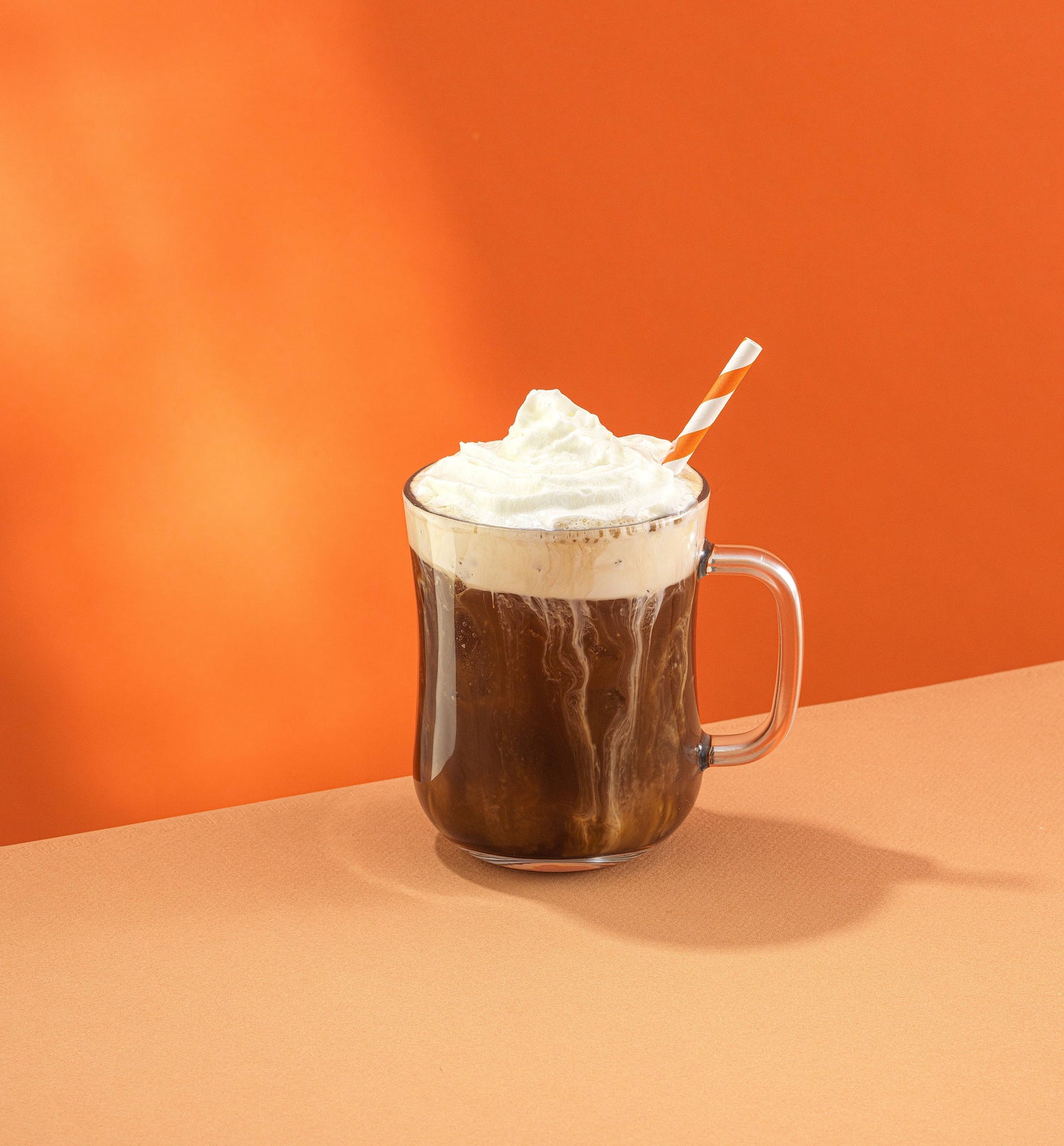 Hot chocolate with whipped cream and a straw on an orange background