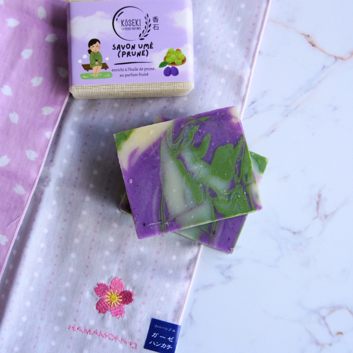 Purple and green soap bars with packaging on a textured surface