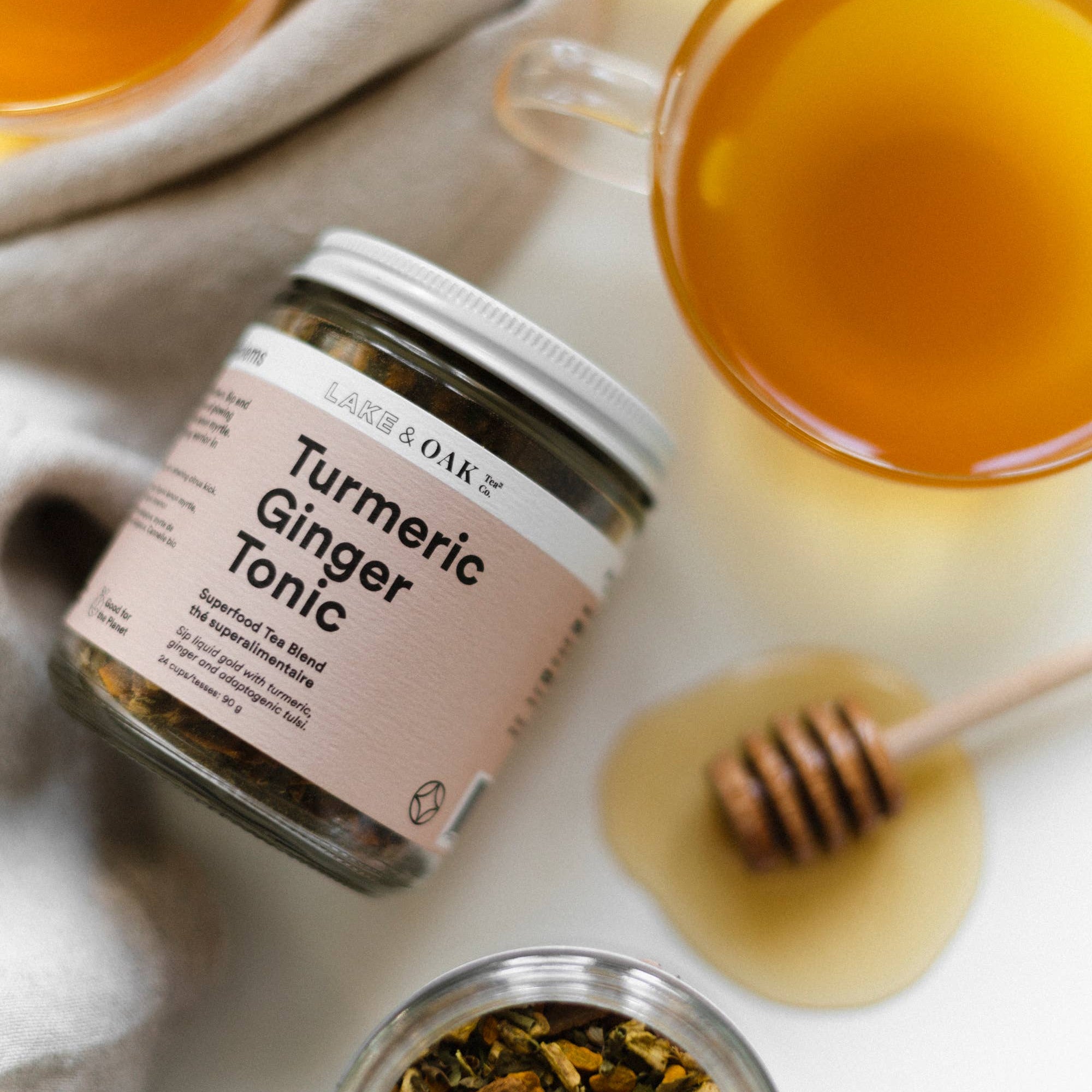 Turmeric Ginger Tonic jar with two glasses of the tonic and a honey dipper on a light background.