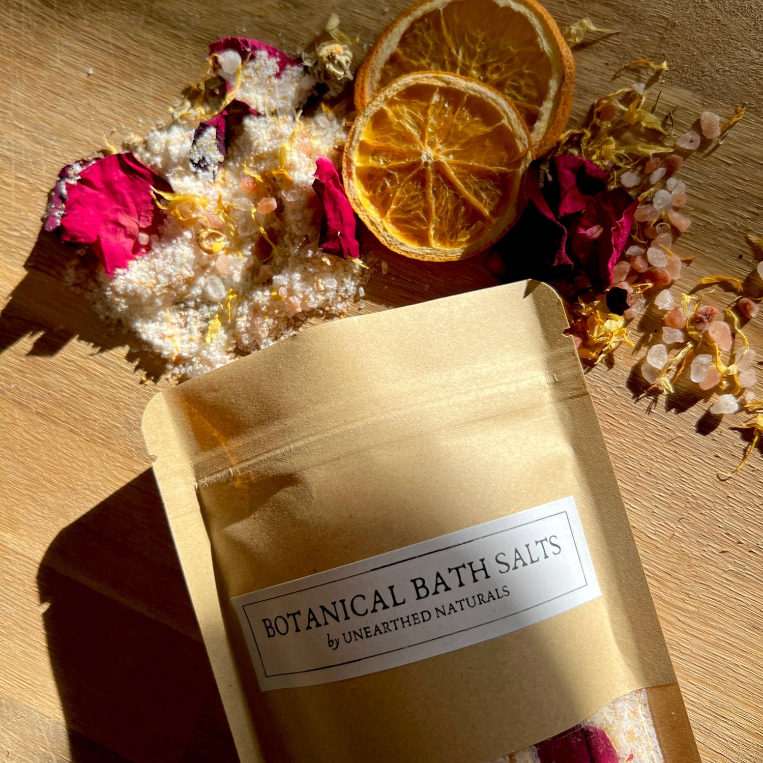 Bag of botanical bath salts with dried flowers and oranges on a wooden surface
