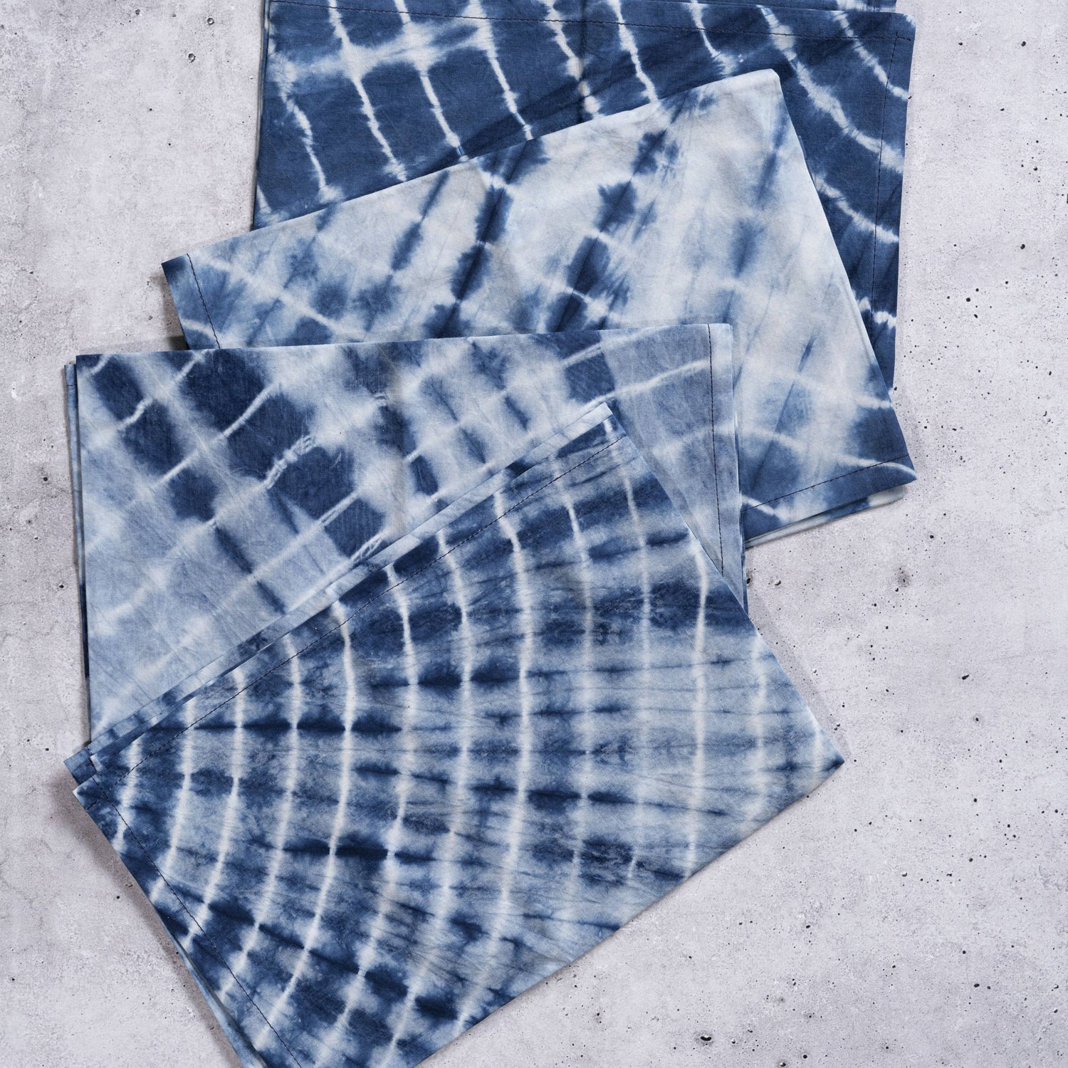 Set of three blue and white tie-dye napkins on a gray surface