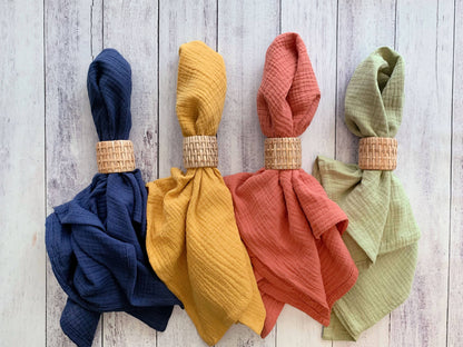Four colorful napkins with rattan napkin rings on a wooden surface