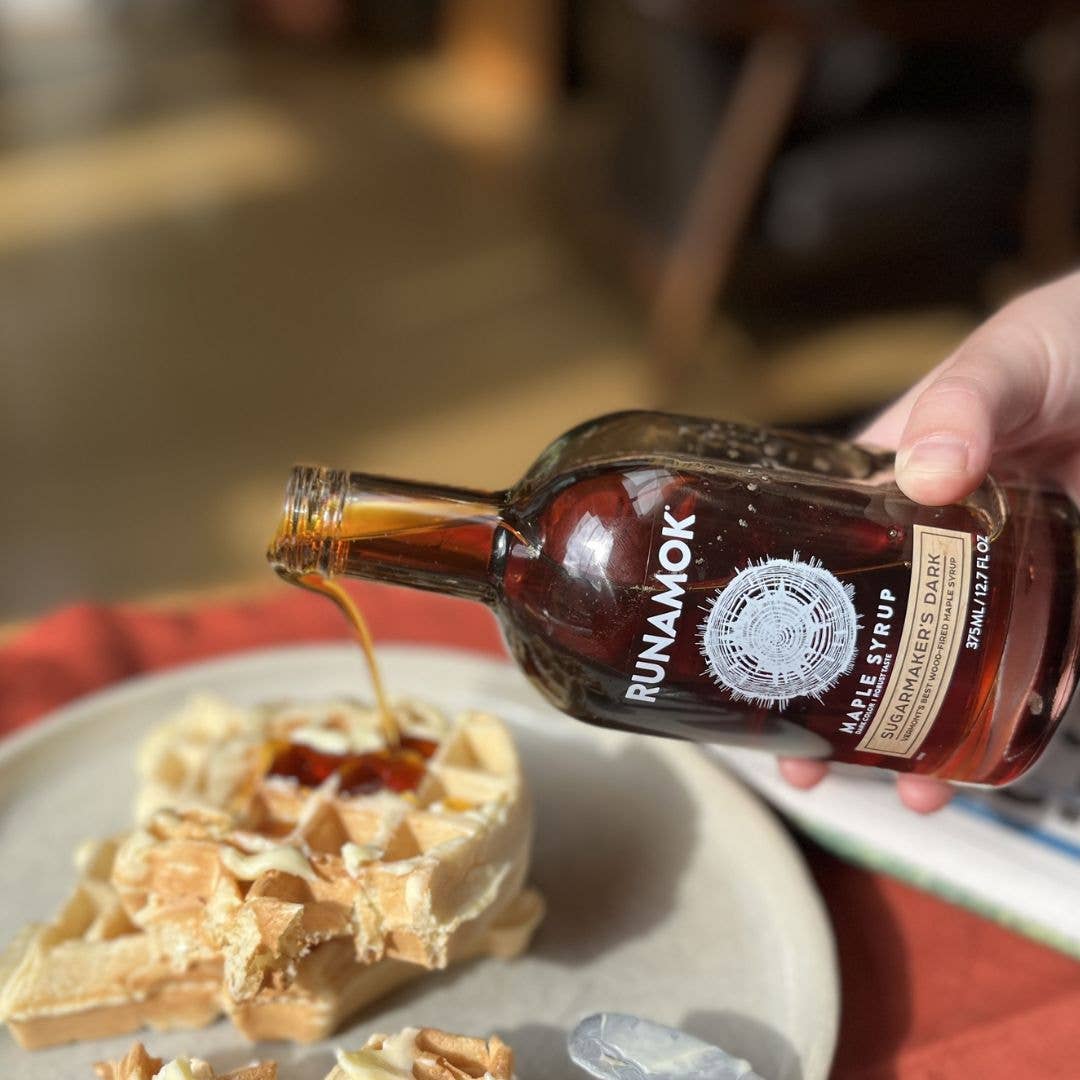 Person pouring Runamok maple syrup onto waffles on a plate.