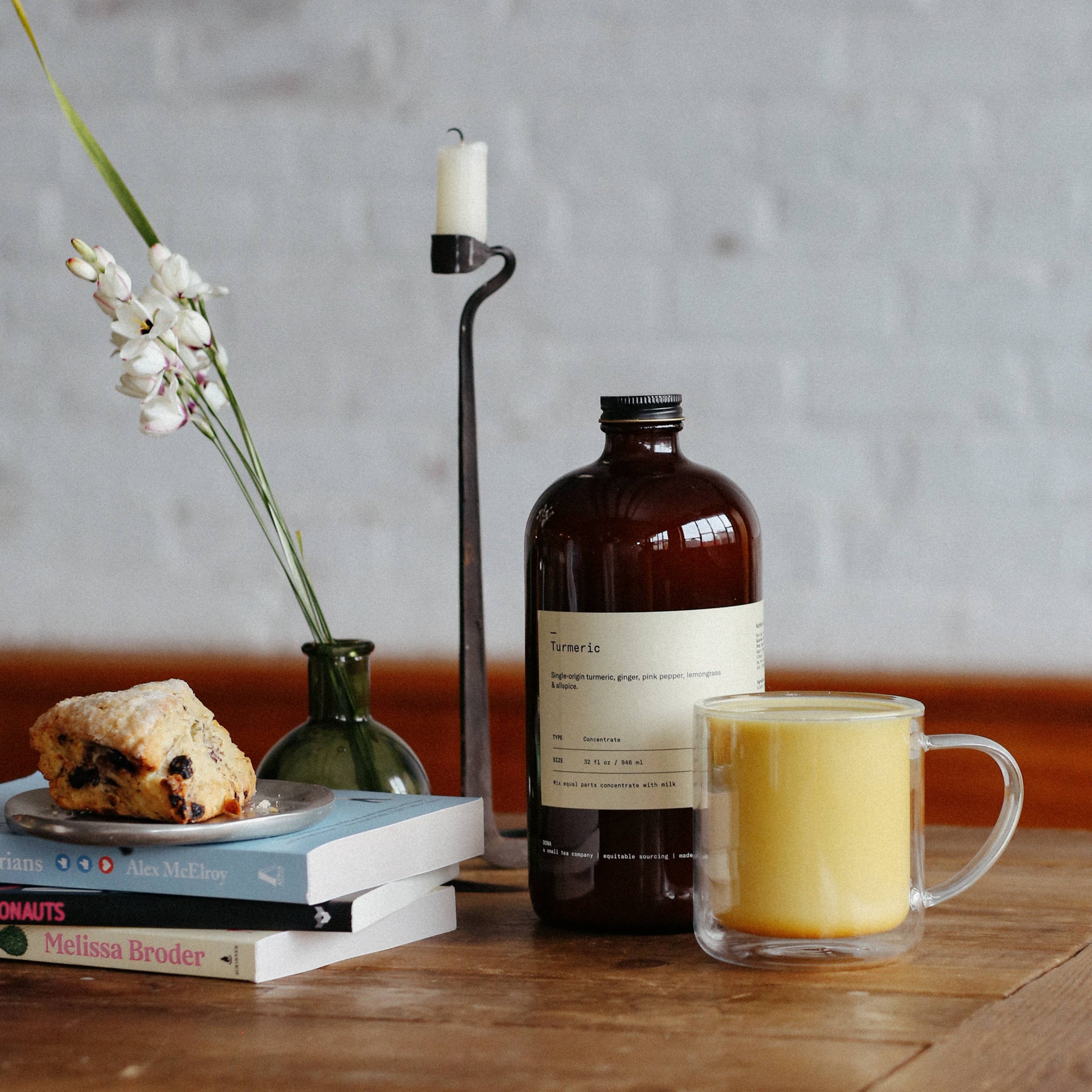 Bottle of Tonic Water, mug with yellow liquid, scone, and candle on a wooden table.