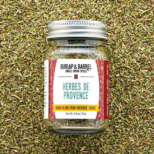 Jar of 'Herbes de Provence' spice blend from Burlap & Barrel on a bed of dried herbs.