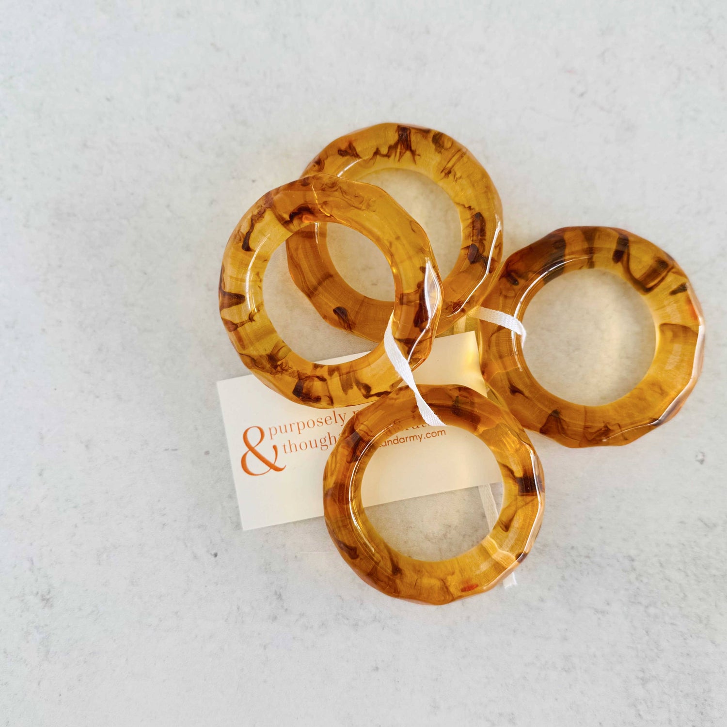 Set of tortoiseshell bangles on a textured white surface with a brand card.