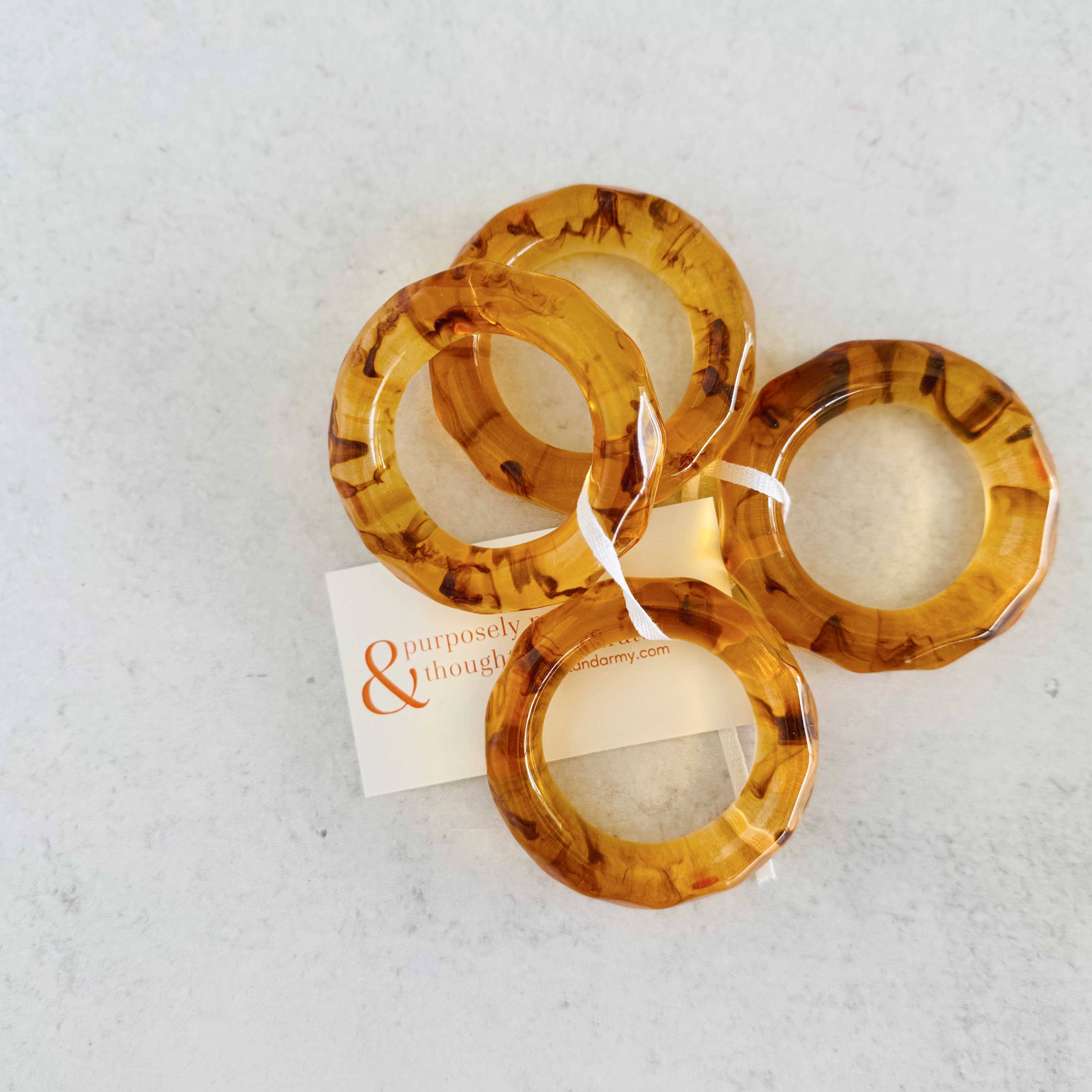 Set of tortoiseshell bangles on a textured white surface with a brand card.