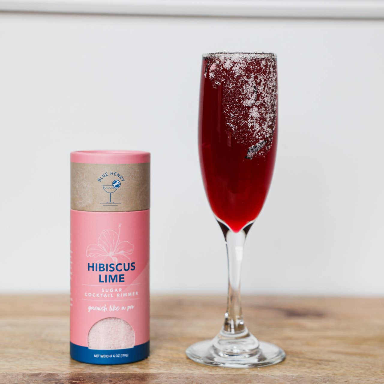 Hibiscus lime sparkling water can next to a glass of red sparkling water on a wooden surface.